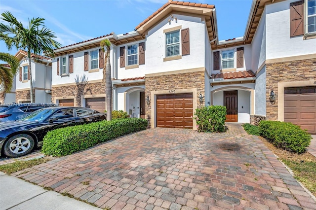 townhome / multi-family property featuring stone siding, decorative driveway, an attached garage, and stucco siding