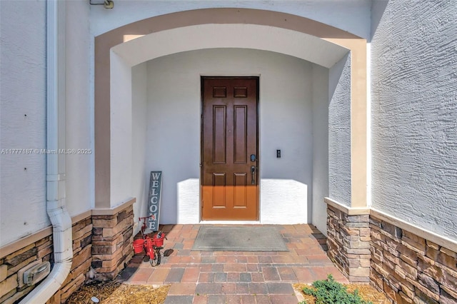 doorway to property featuring stucco siding and stone siding