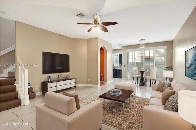 living area with light tile patterned floors, visible vents, a ceiling fan, and arched walkways