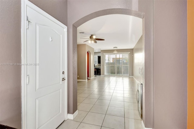 corridor featuring light tile patterned flooring, arched walkways, visible vents, and baseboards