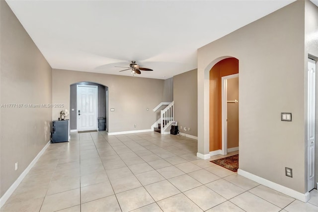 unfurnished room featuring stairway, a ceiling fan, light tile patterned floors, and arched walkways