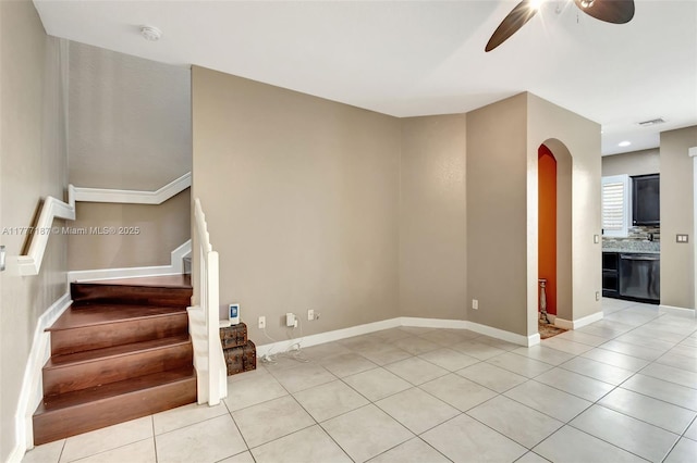 unfurnished living room featuring light tile patterned floors, ceiling fan, stairs, baseboards, and arched walkways
