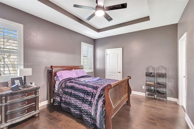 bedroom featuring baseboards, wood finished floors, multiple windows, and a tray ceiling