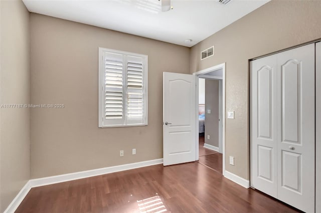unfurnished bedroom featuring visible vents, baseboards, dark wood-style floors, and a closet