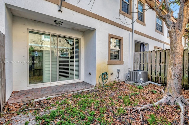 entrance to property featuring stucco siding, fence, and central AC