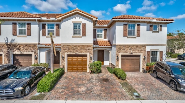 multi unit property featuring driveway, a tile roof, stone siding, an attached garage, and stucco siding
