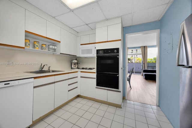kitchen with white appliances, light countertops, a sink, white cabinetry, and a paneled ceiling
