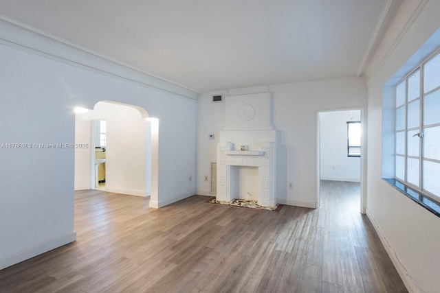 unfurnished living room featuring arched walkways, visible vents, wood finished floors, and baseboards