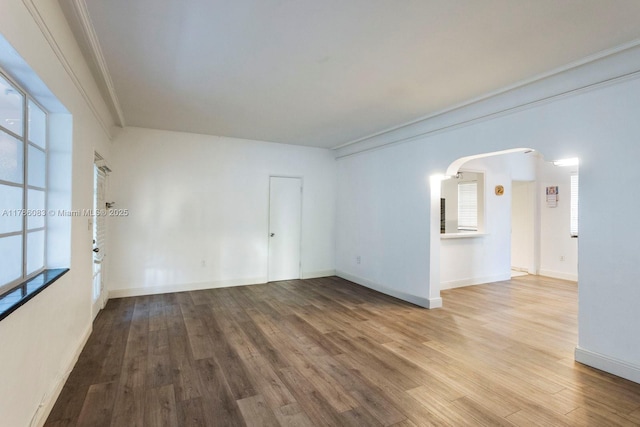 unfurnished room featuring ornamental molding, arched walkways, wood finished floors, and baseboards