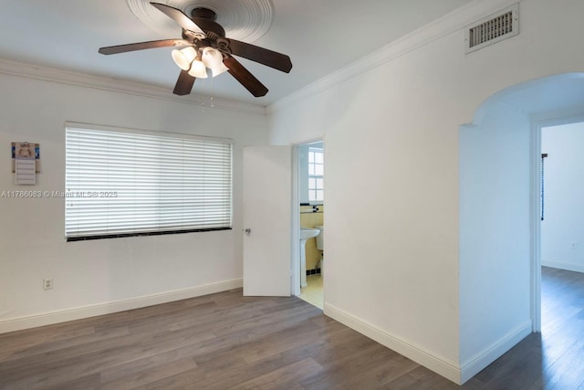 spare room with ceiling fan, crown molding, visible vents, arched walkways, and wood finished floors