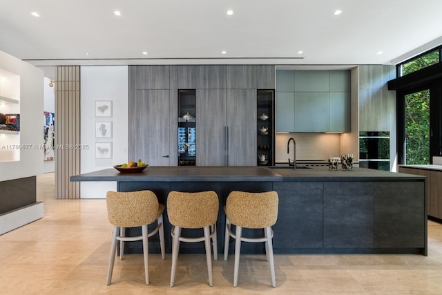 kitchen featuring dark countertops, a sink, a breakfast bar area, a large island with sink, and modern cabinets