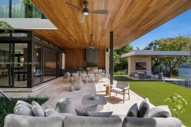 view of patio / terrace with a water view, ceiling fan, an outdoor living space with a fireplace, and area for grilling
