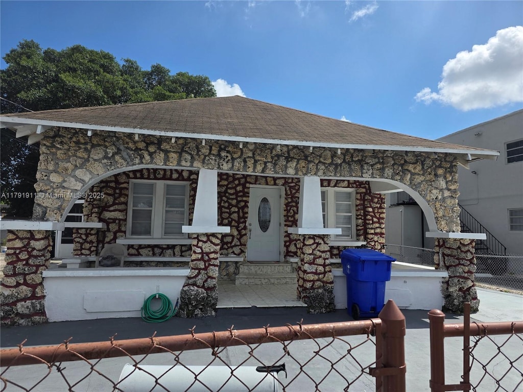 view of front of house with stone siding, fence, a porch, and roof with shingles