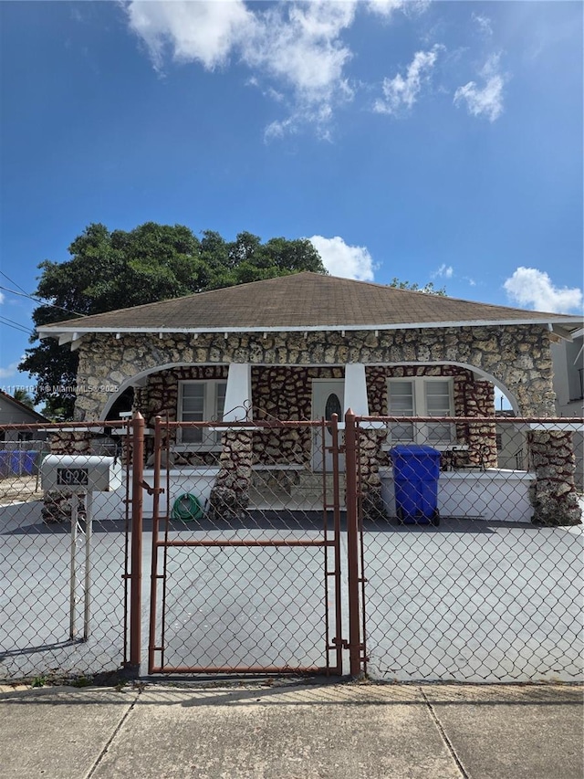 view of front of home with a gate, stone siding, a fenced front yard, and roof with shingles