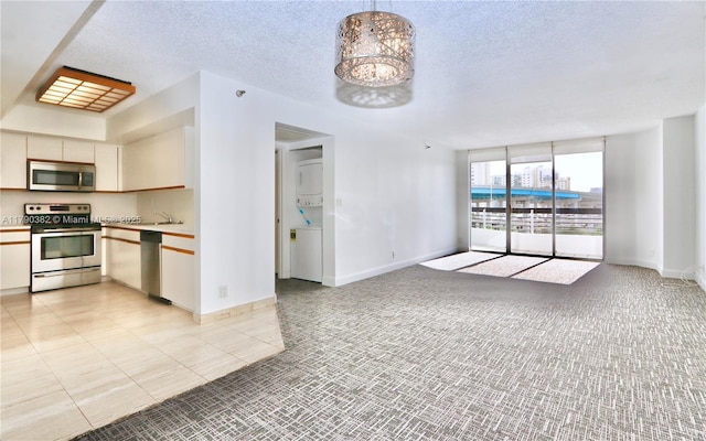 kitchen featuring light colored carpet, stainless steel appliances, stacked washer and dryer, and light countertops