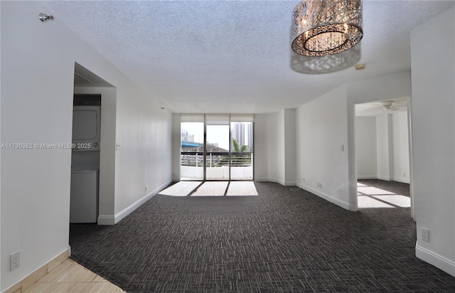 unfurnished room featuring stacked washer and dryer, a textured ceiling, baseboards, carpet, and a notable chandelier