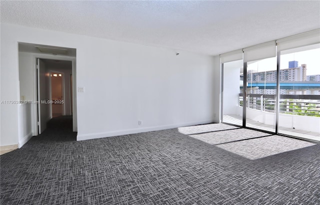 spare room featuring baseboards, dark colored carpet, a textured ceiling, and expansive windows