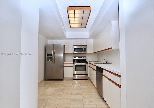 kitchen featuring a sink, stainless steel appliances, light tile patterned floors, light countertops, and white cabinets