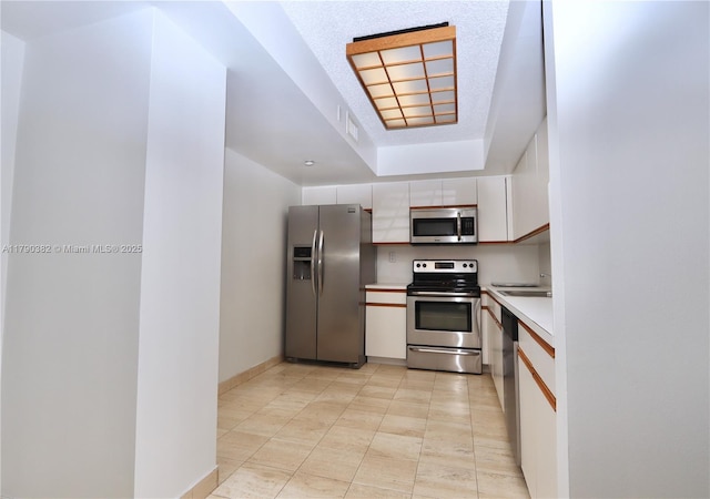 kitchen featuring appliances with stainless steel finishes, light countertops, white cabinets, baseboards, and a tray ceiling
