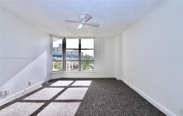 spare room with baseboards, dark colored carpet, a ceiling fan, and a textured ceiling
