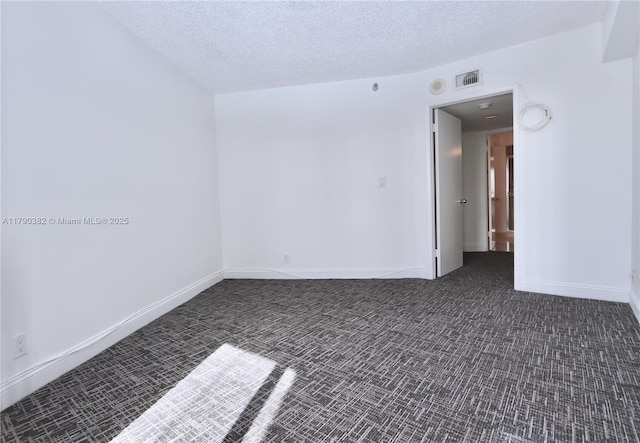 empty room with baseboards, visible vents, dark colored carpet, and a textured ceiling