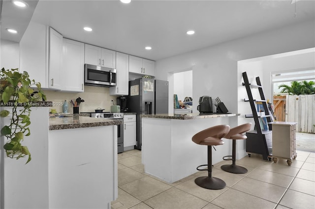 kitchen featuring light tile patterned floors, appliances with stainless steel finishes, white cabinets, backsplash, and a kitchen bar