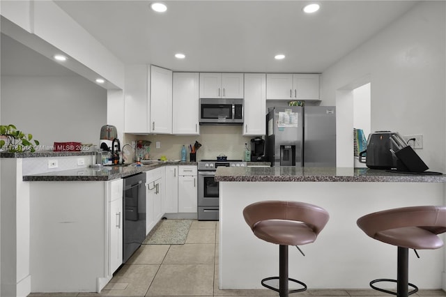kitchen featuring white cabinetry, appliances with stainless steel finishes, a kitchen bar, recessed lighting, and a peninsula