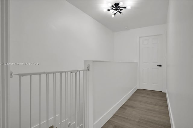 hall featuring baseboards, wood finished floors, an inviting chandelier, and an upstairs landing