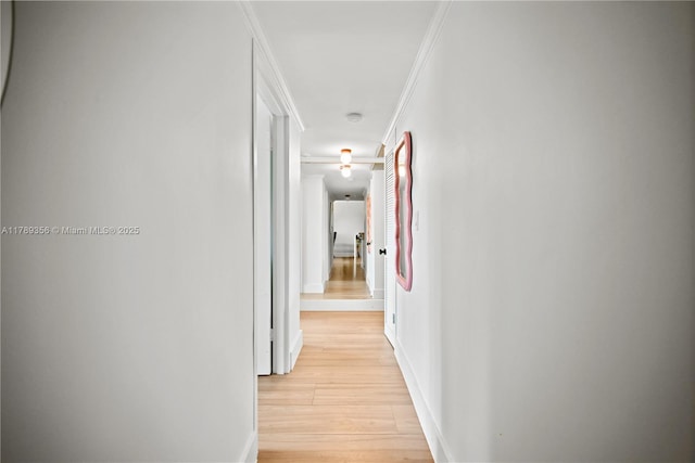 hall with baseboards, crown molding, and light wood finished floors