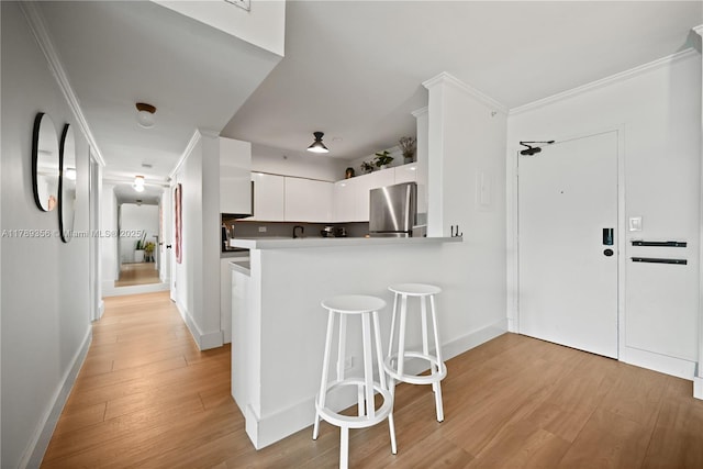 kitchen with light wood-style floors, a kitchen bar, ornamental molding, white cabinets, and freestanding refrigerator