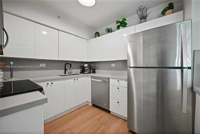 kitchen featuring white cabinets, a sink, stainless steel appliances, light countertops, and light wood-type flooring