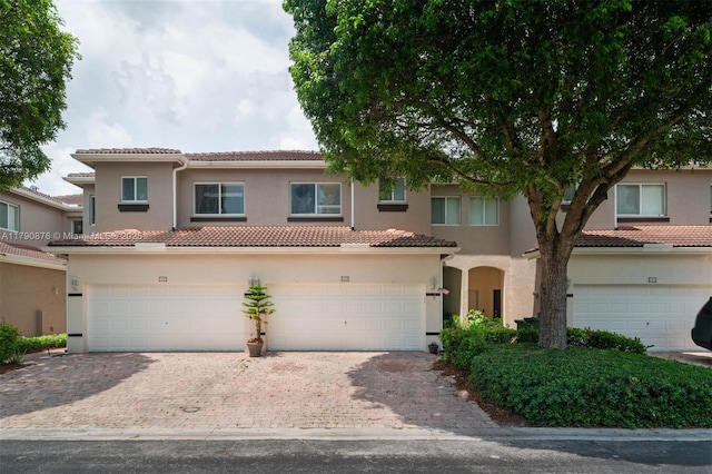 view of front facade with stucco siding, decorative driveway, a tiled roof, and a garage