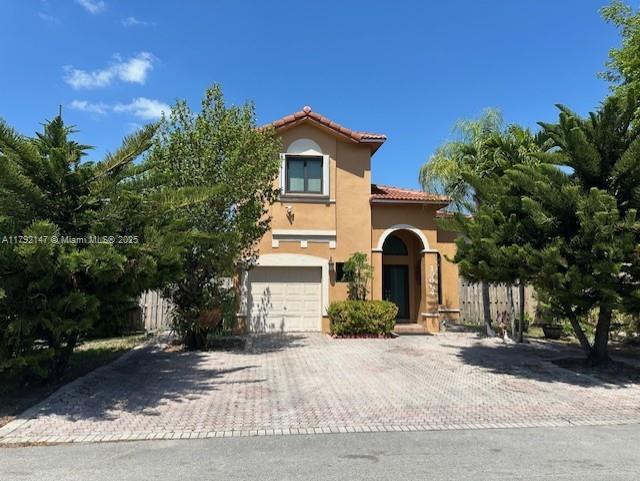 mediterranean / spanish-style home featuring fence, a tile roof, a garage, stucco siding, and decorative driveway