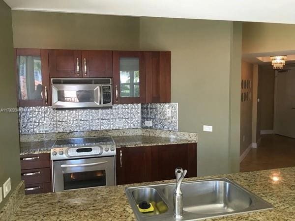 kitchen featuring a sink, decorative backsplash, glass insert cabinets, light stone counters, and appliances with stainless steel finishes