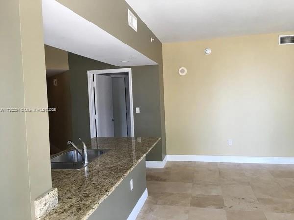 interior space featuring visible vents, stone countertops, baseboards, and a sink