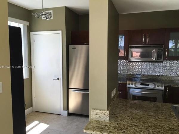 kitchen with dark stone counters, appliances with stainless steel finishes, baseboards, an inviting chandelier, and backsplash