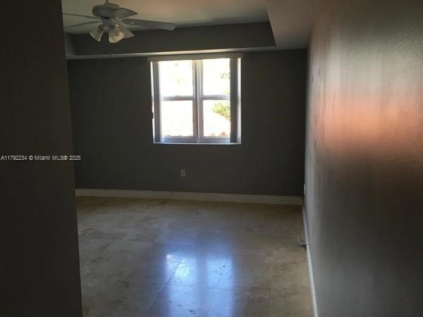 spare room with a ceiling fan and baseboards