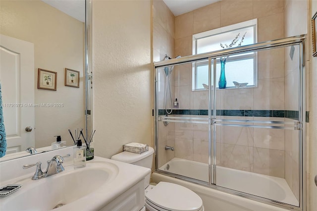 full bathroom with combined bath / shower with glass door, a textured wall, toilet, and vanity