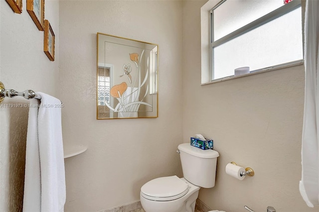 bathroom with baseboards, a healthy amount of sunlight, and toilet