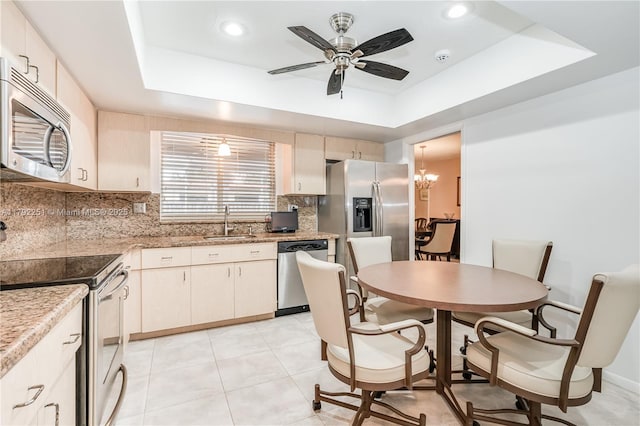 kitchen featuring a ceiling fan, tasteful backsplash, a sink, a raised ceiling, and stainless steel appliances