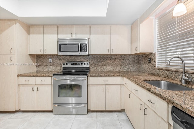 kitchen featuring backsplash, appliances with stainless steel finishes, light stone countertops, a sink, and light tile patterned floors