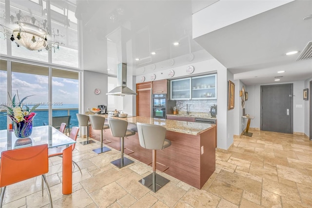 1830 S Ocean Dr Unit 1201, Hallandale Beach, FL 33009 - kitchen featuring a breakfast bar area, dobule oven black, range hood, glass insert cabinets, and stone tile flooring