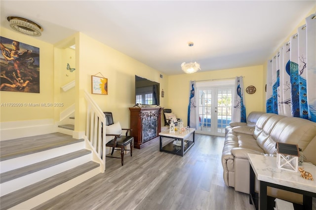 living area with light wood-type flooring, an inviting chandelier, french doors, and stairway