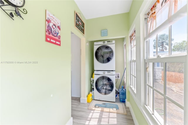 laundry area featuring baseboards, stacked washer / dryer, and wood finished floors
