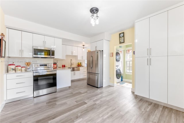 kitchen with stacked washer / drying machine, light wood-style floors, appliances with stainless steel finishes, light countertops, and white cabinets