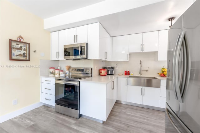 kitchen featuring white cabinetry, a sink, stainless steel appliances, light countertops, and light wood finished floors