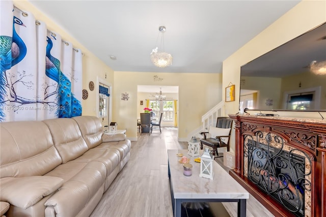 living room featuring baseboards, stairway, a notable chandelier, and light wood finished floors