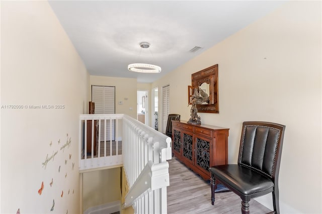 hallway featuring light wood-style floors, visible vents, and an upstairs landing