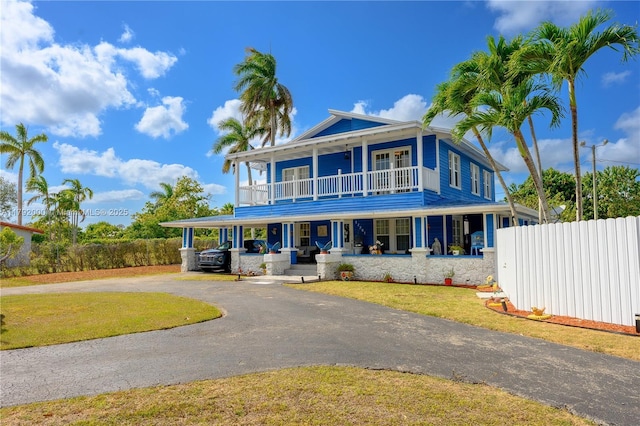 view of front of house with driveway, a balcony, fence, a porch, and a front lawn