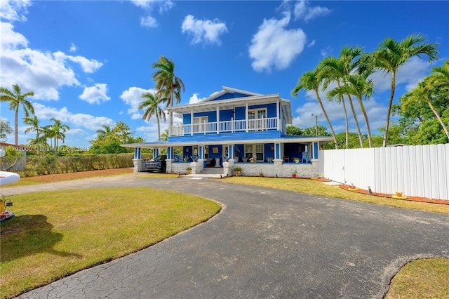 view of front of home featuring a balcony, covered porch, a front yard, curved driveway, and fence